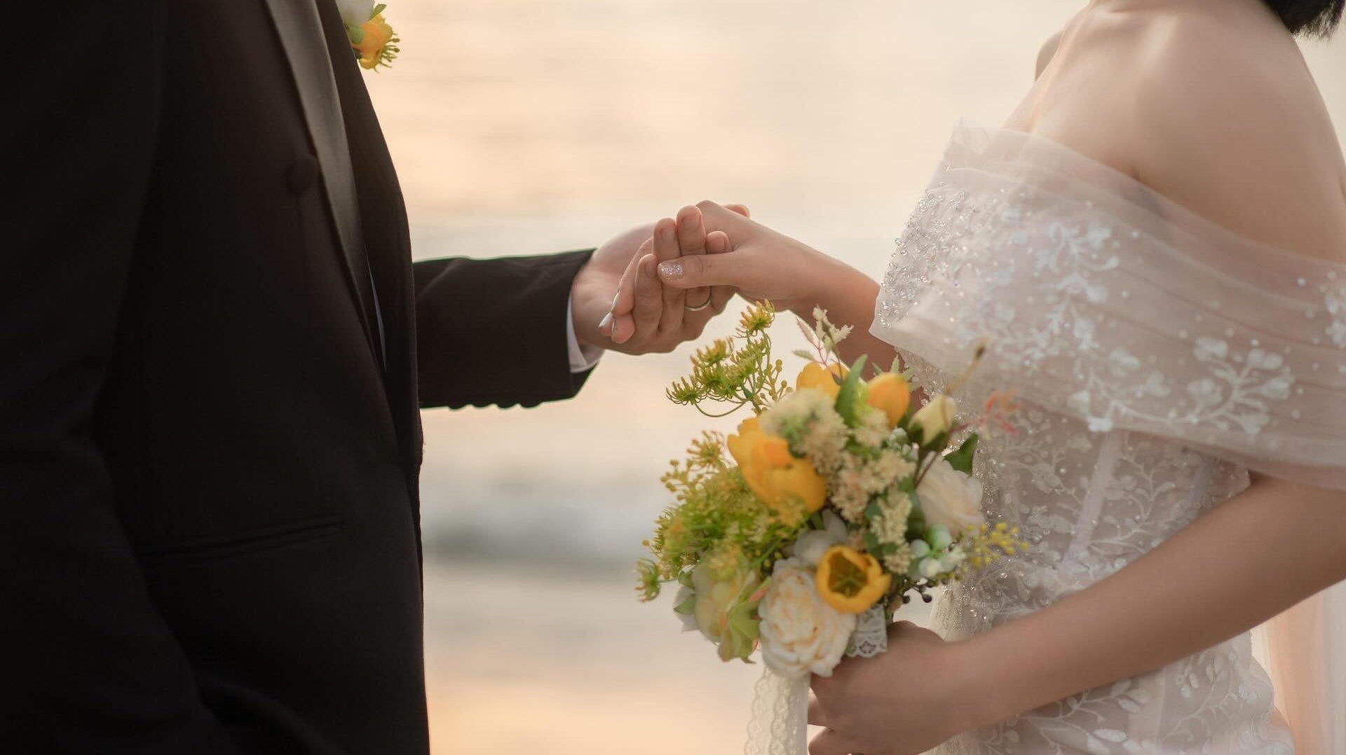 Wedding couple holding hands while looking at each other on a beach.