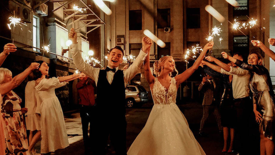 Wedding couple walking downtime street with their guests creating a guard of honour with sparklers