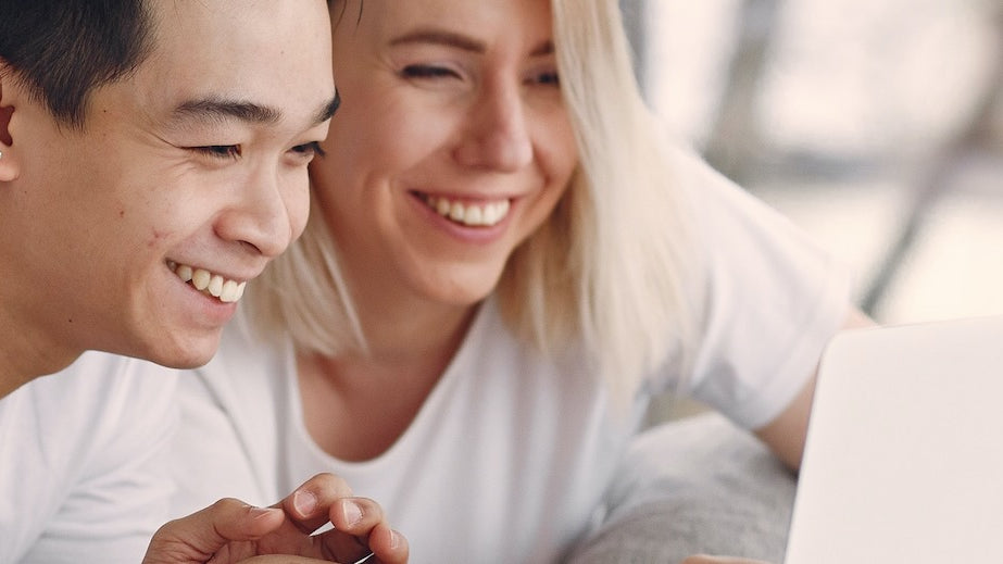 A happy young couple are both looking at a laptop computer smiling.
