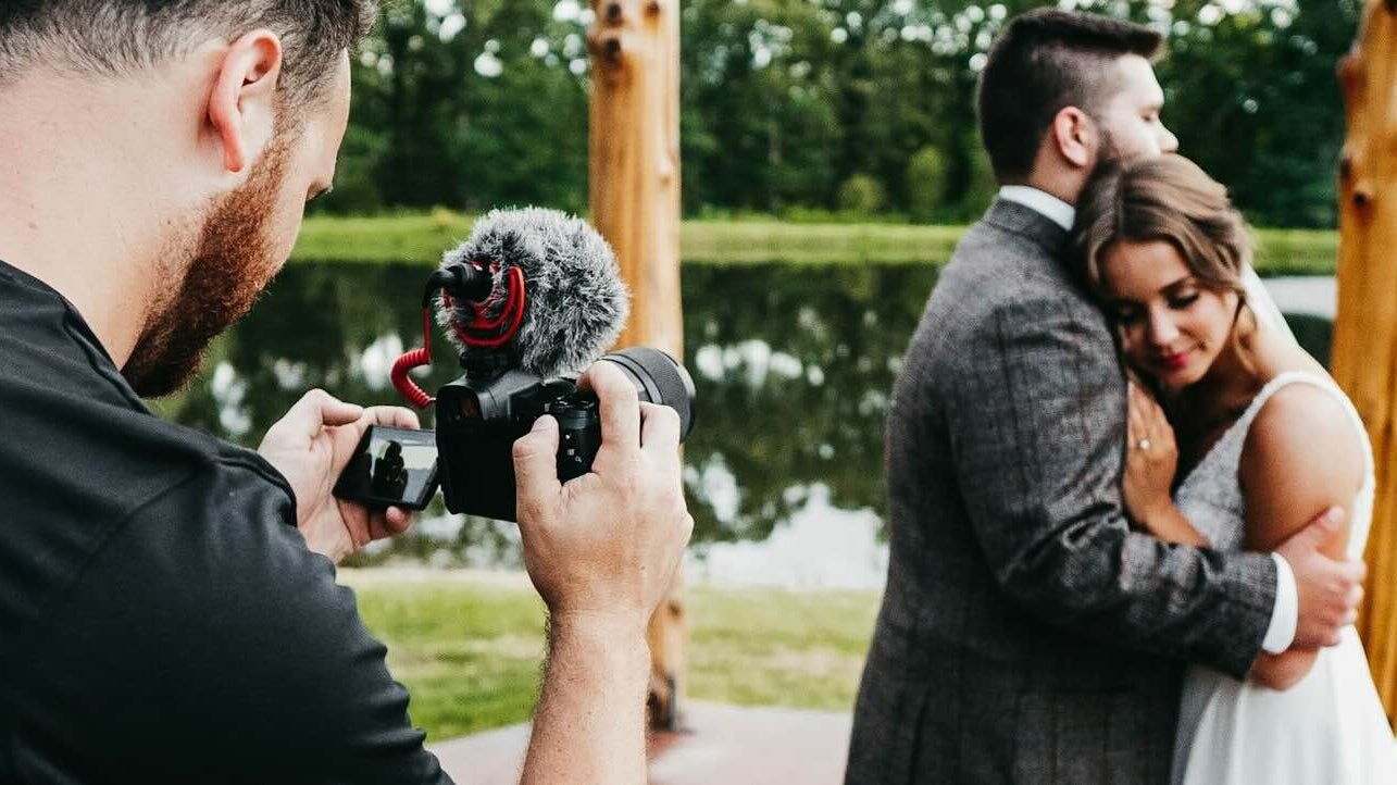 Wedding couple being video recorded by a man holding camera.