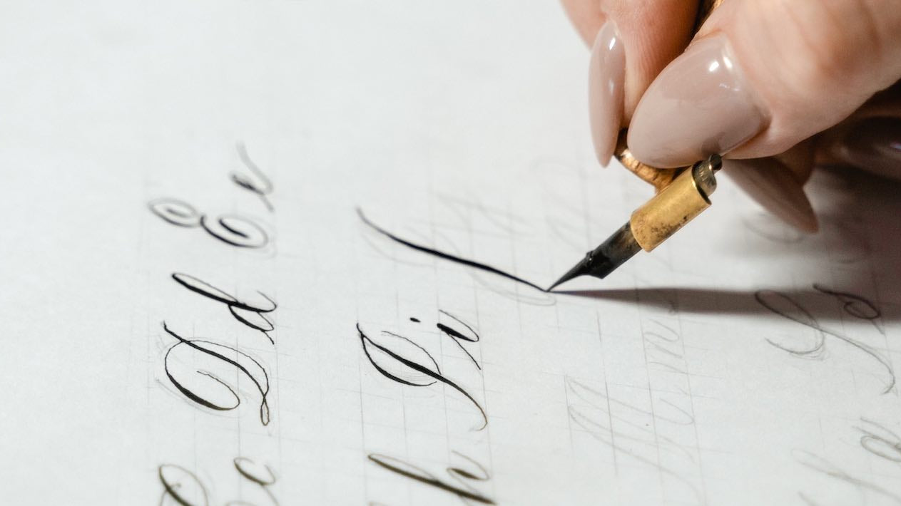 female hand holding an ink calligraphy pen and writing alphabet characters