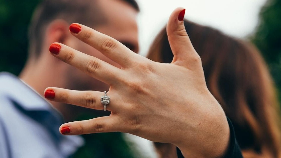 Woman standing next to a man holding up her engagement ring.
