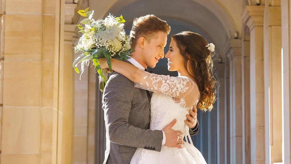 Bride and groom gaze into each others eyes in front of a period archway of a castle.