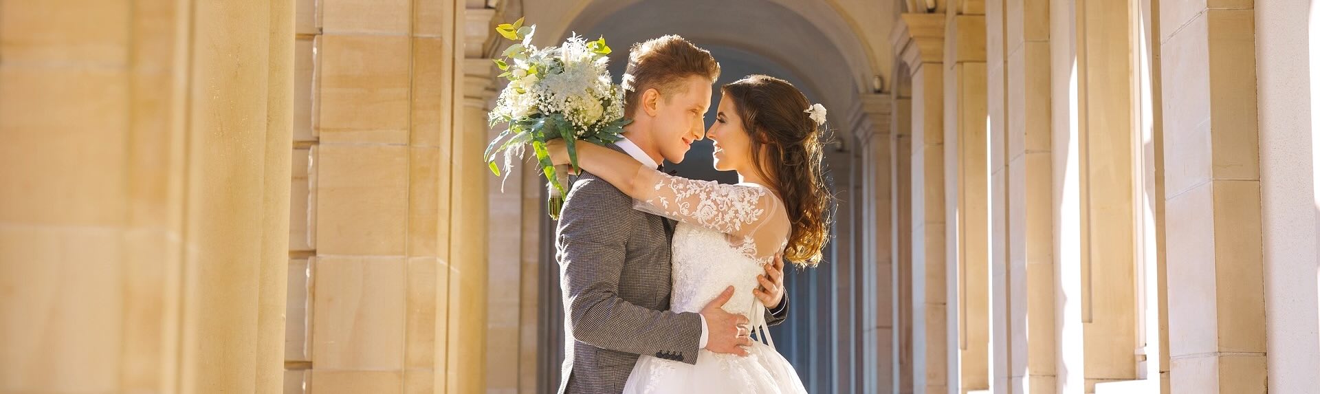 Bride and groom gaze into each others eyes in front of a period archway of a castle.