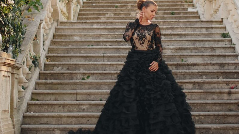 Woman in elegant black gown poses as the bottom of a stair case.