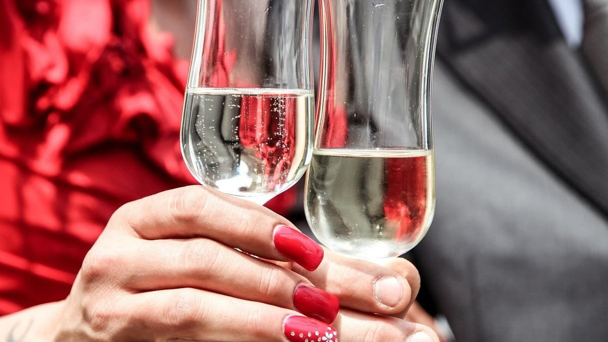 Man and woman clink champaign glasses while wearing formal clothing.