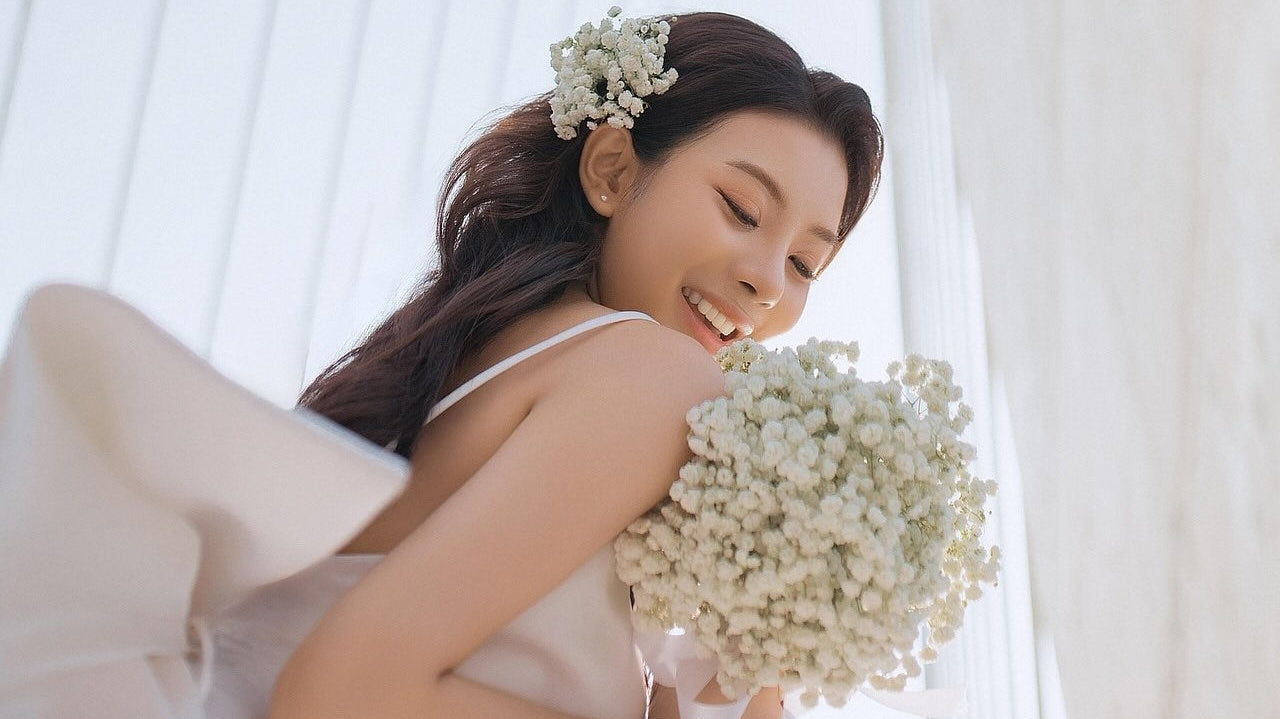 Bride smiles and looks down at her white wedding bouquet.