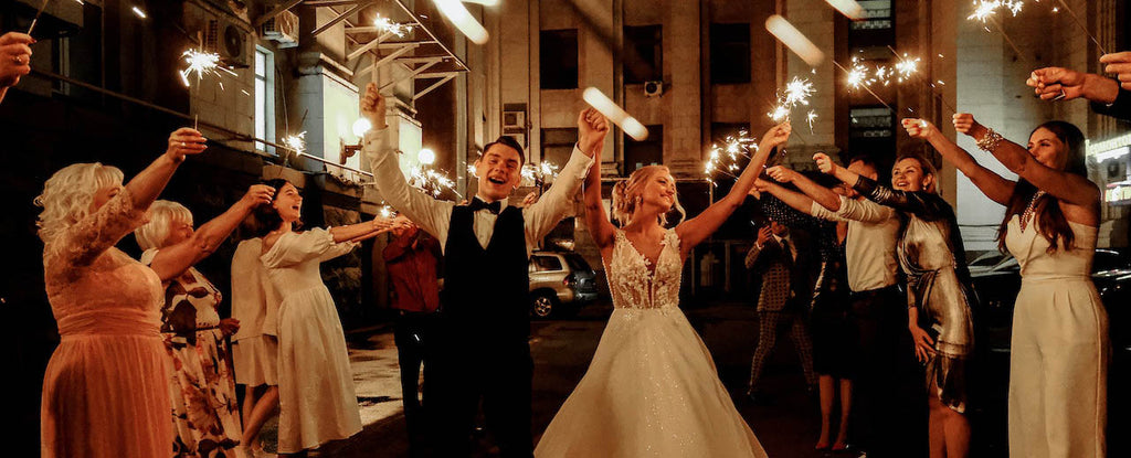 Wedding couple walking downtime street with their guests creating a guard of honour with sparklers