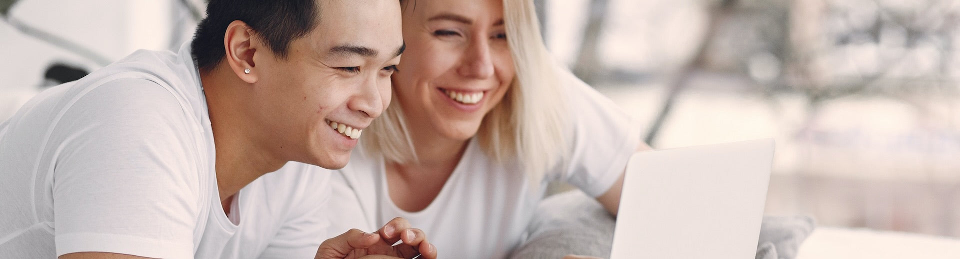 A happy young couple are both looking at a laptop computer smiling.