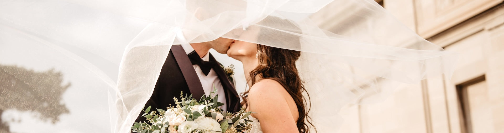 Couple getting married kissing under brides veil. 