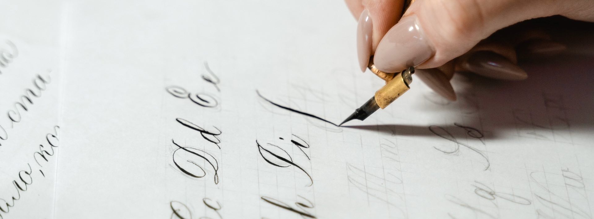 female hand holding an ink calligraphy pen and writing alphabet characters