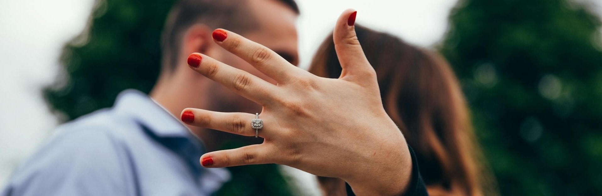 Woman standing next to a man holding up her engagement ring.