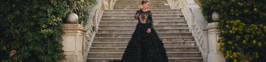 Woman in elegant black gown poses as the bottom of a stair case.