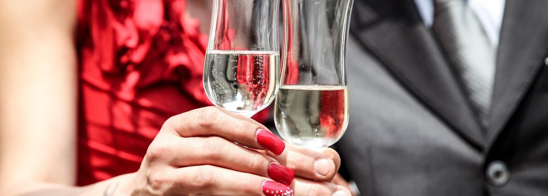 Man and woman clink champaign glasses while wearing formal clothing. 