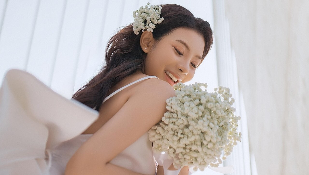 Bride smiles and looks down at her white wedding bouquet. 