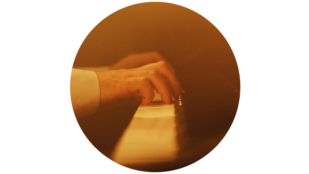 Close up of hands playing a piano. With a yellow light shining over the top