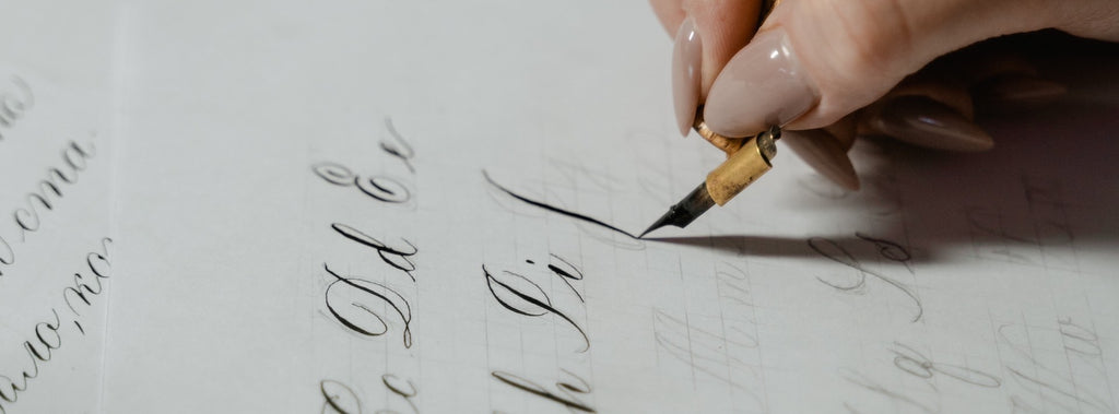 close up of a hand holding a traditional ink pen writing out the alphabet in calligraphy writing