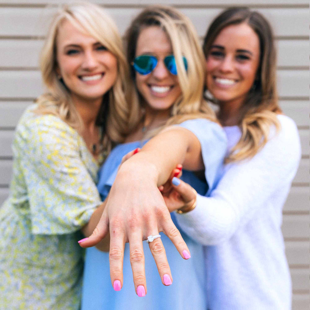 Engaged woman with engagement ring stands with two friends